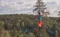 A tightrope walker walks along a long highline above the forest. Back view