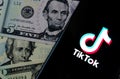 TikTok app logo on the smartphone screen and US dollar bills next to it. Conceptual photo