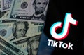 TikTok app logo on the smartphone screen and US dollar bills next to it. Conceptual photo