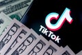 TikTok app logo on the smartphone screen and US dollar bills next to it. Conceptual photo