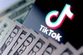 TikTok app logo on the smartphone screen and US dollar bills next to it. Conceptual photo