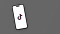 Tiktok Logo on Mobile Phone Screen on Gray Background with Copy Space