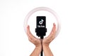 The tiktok logo on a smartphone attached to a round lamp with a tripod and male hands show protection. Donald Trump to ban Tiktok