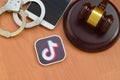 Tiktok paper logo lies with wooden judge gavel, smartphone and handcuffs. Entertainment lawsuit concept