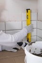 The tile installation wizard measures the correct laying of white tiles, using the yellow level, close-up Royalty Free Stock Photo