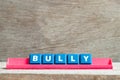 Tile letter on rack in word bully on wood background