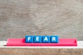 Tile letter on rack in word fear on wood background