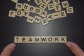 Tile letters fingers spelling teamwork on a black background with mixed letters on top. Concept for business, personal, team