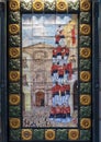 Tile painting with a column of men standing on each other`s shoulders on the outside of a business along a sidewalk in Barcelona.