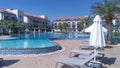 The tiled area near the swimming pool, surrounded by buildings with balconies and palm trees, is lined with plastic and fabric umb Royalty Free Stock Photo