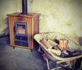 Tiled stove and wheelbarrow full of firewood with vintage effect