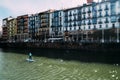 Tilt shift selective focus effect on person on standup paddle on the Nervion River in Bilbao, Spain with traditional buildings on