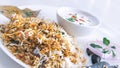 Tilt shot of delicious Indian Hyderabadi biryani with curd and salad in a white background