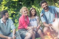 Tilt shot of smiling family with male friend roasting sausages over campfire at park