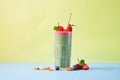 tilted angle: spinach berry smoothie in a tall glass, against a brightly colored background