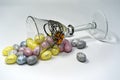 Easter composition: pastel mini eggs in a glass goblet decorated with metal and amber. Bright background.