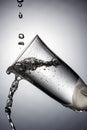 Tilted champagne glass close-up with frozen water jets and splashes in white backlight. Stop motion photography