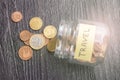 Tilted glass jar with scattered euro coins with the inscription TRAVEL on a black wooden table