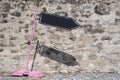 Tilted pink road sign with black board arrow showing direction. Wall background in sunny day.