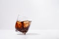 Tilted transparent glass with cola wave and ice on white isolated background on daylight. Place for your design