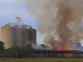 Timber shed on fire burnng under Grain silos Royalty Free Stock Photo