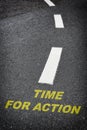 Time for action written on black asphalt road and white marking lines