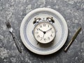 Time for breakfast. Alarm clock in a plate, fork and knife on a concrete table. Top view. Flat lay Royalty Free Stock Photo