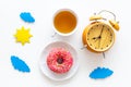 Time for breakfast concept. Tea, donut near alarm clock, sun and clouds cutout on white background top view Royalty Free Stock Photo