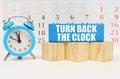 Against the background of the calendar, an alarm clock and a blue block with the inscription - Turn Back the Clock