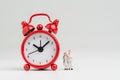 Time counting down for retirement concept, miniature happy senior old couple standing with big red alarm clock on white background