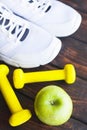 Time for diet slimming weight loss concept. Sport fitness, apple, sneakers, bottle of water and yellow weights on dark wooden back Royalty Free Stock Photo