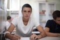 Teenagers students sitting in the classroom and writing. Male looking at camera. Focus is on foreground Royalty Free Stock Photo