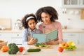 Black woman and girl cooking in kitchen reading recipe book