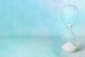 Time. An hourglass with flowing sand on a pastel blue background