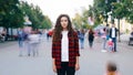 Time-lapse portrait of serious girl hipster standing still in street downtown, looking at camera when bypassers are