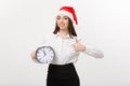 Time management concept - Young business woman with santa hat holding a clock and showing thump up isolated over white Royalty Free Stock Photo