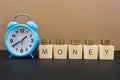 Time is money concept with alarm clock, coins and the word written on wooden cubes. A valuable resource for making money in busine