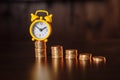 Time is money concept. An alarm clock and stack of coins on a wooden table Royalty Free Stock Photo