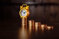 Time is money concept. An alarm clock and stack of coins on a wooden table Royalty Free Stock Photo