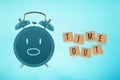 TIME OUT text on wooden cubes with shocked face alarm clock on blue background