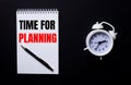 TIME FOR PLANNING is written in a white notepad near a white alarm clock on a black background Royalty Free Stock Photo