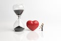 Time prove love for couple concept, with sandglass or hourglass, red shiny ceramic heart shape and miniature couple holding each
