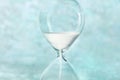 Time is running out concept. A close-up of an hourglass with sand falling through, on a teal blue background
