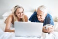 Time for some leisurely browsing. a mature couple using a laptop while relaxing on their bed at home. Royalty Free Stock Photo
