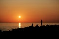 Time of sunset on the Black Sea. Silhouettes of pyramids of stones on the shore and men. Orange color.