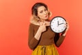 Time to act! Punctual woman pointing finger at white display of big wall clock seriously looking at camera