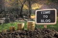 Time To Blog concept. Golden coins in soil Chalkboard on blurred natural background