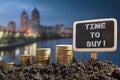 Time to buy - Financial opportunity concept. Golden coins in soil Chalkboard on blurred urban background Royalty Free Stock Photo