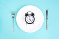 Time to eat. Lunch time. View from above on white plate with alarm clock and knife and pork near on blue background. 5 p Royalty Free Stock Photo