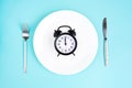 Time to eat. Lunch time. View from above on white plate with alarm clock and knife and pork near on blue background. 12 Royalty Free Stock Photo